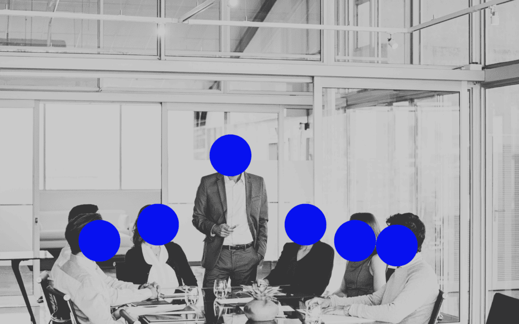 A monochrome photo captures a media buyer speaking passionately to five colleagues in a conference room. The others, likely from the media buying agency, are seated around a table, listening intently.